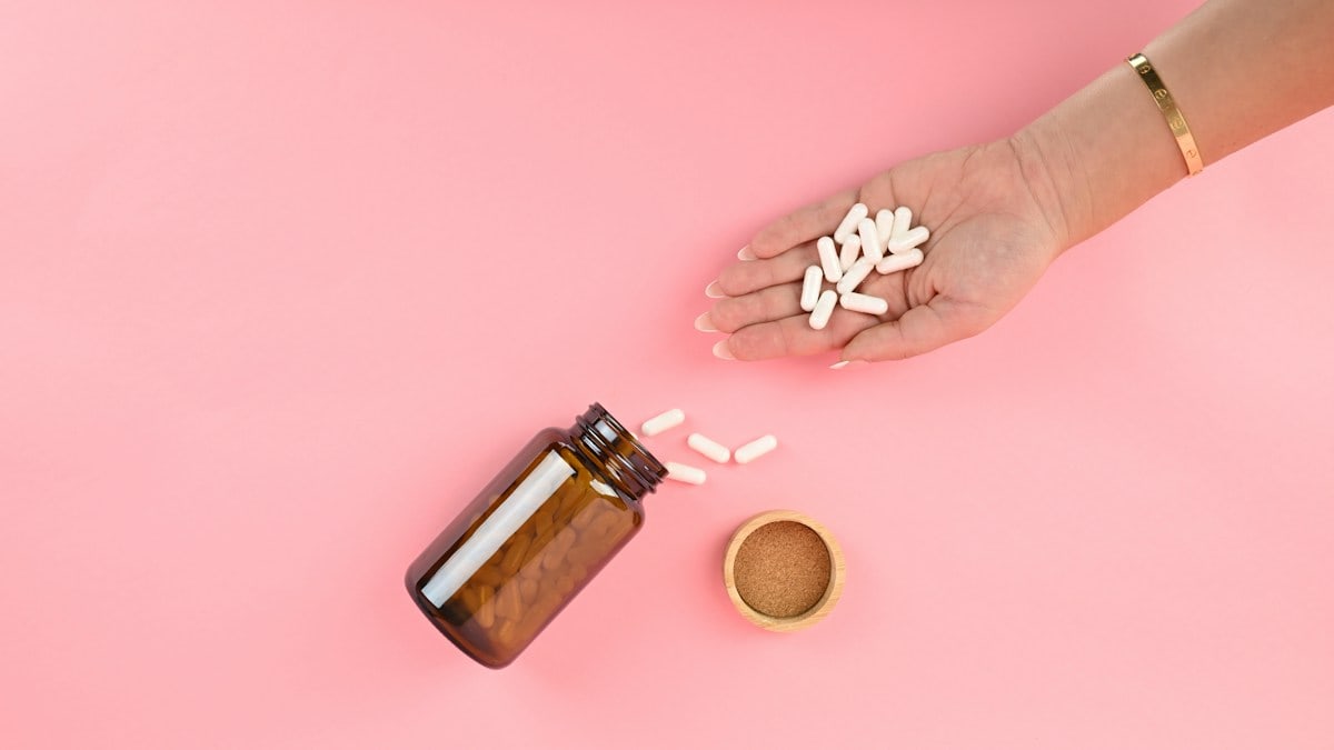 Woman's hand holding handful of white capsules with amber glass pill bottle - Image courtesy of Blated®: https://blated.com (credit appreciated)